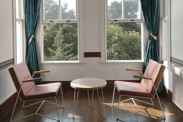 An empty consulting room in daylight, two chairs facing each other by tall windows